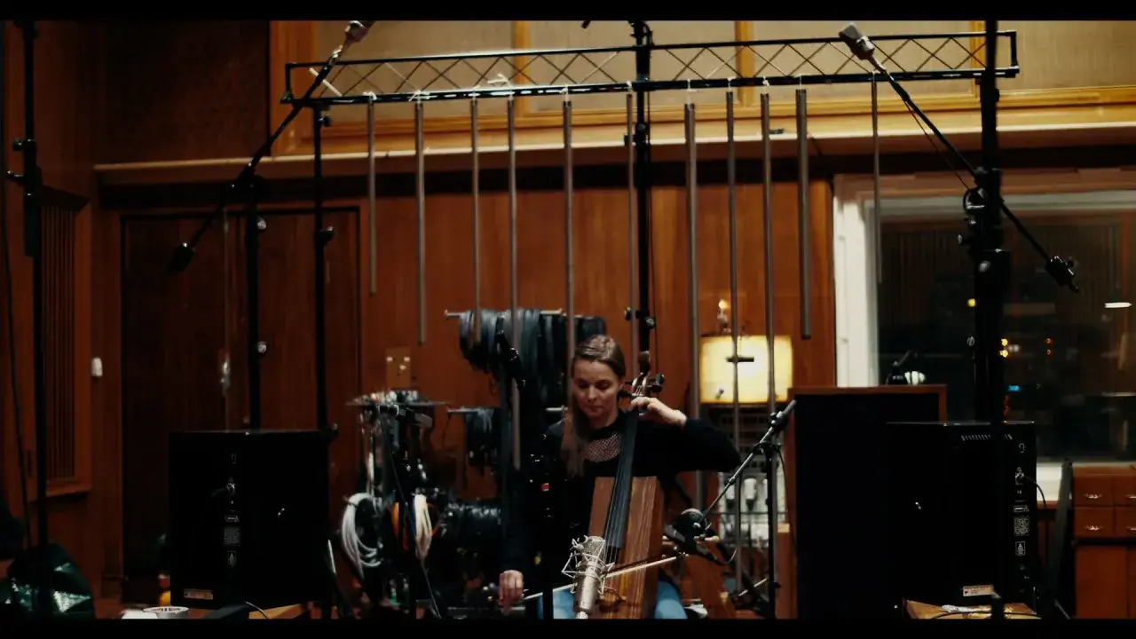 Una violonchelista graba la banda sonora de Joker en un estudio de grabación, rodeada de micrófonos y equipo.