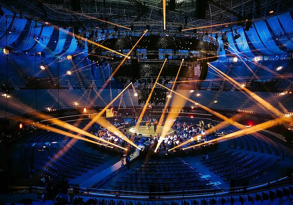 Un concierto con luces naranjas cruzándose sobre un escenario circular. La orquesta y el público están sentados, pero el bad sound system arruina la experiencia.