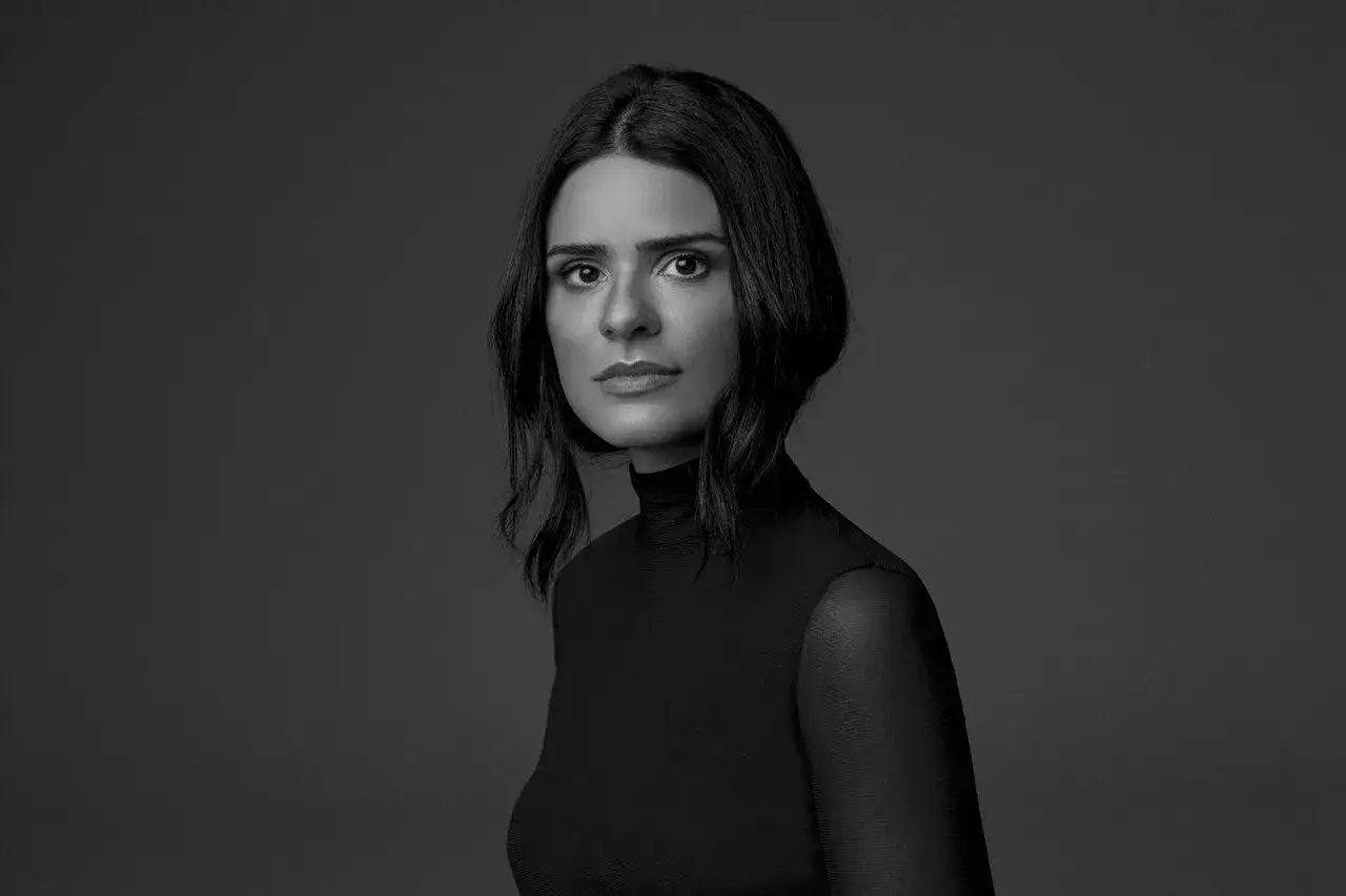 Anna DJ, con mirada intensa y cabello oscuro, posa con un elegante vestido negro de cuello alto.