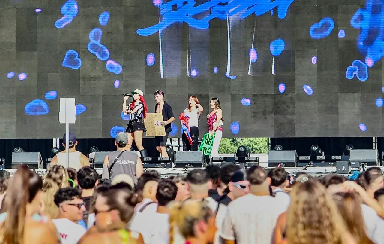 Artistas en el escenario, con público al frente. La cantante principal, con pelo rojo, canta. Podría ser un concierto de Nicky Jam en Granada.