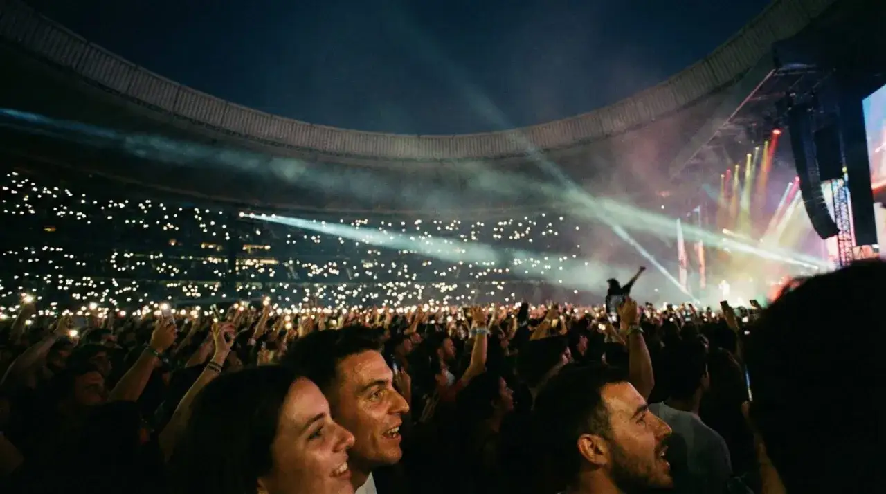 Multitud en conciertos Madrid, con móviles encendidos creando un mar de luces. El escenario ilumina la noche.
