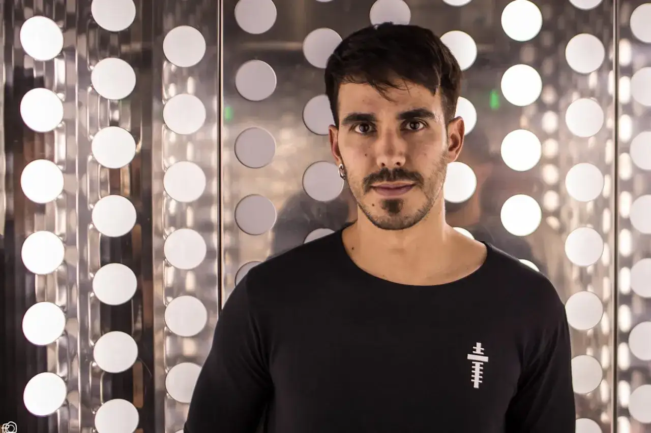 Raúl Pacheco DJ, con su mirada intensa, posa frente a un fondo de círculos luminosos.