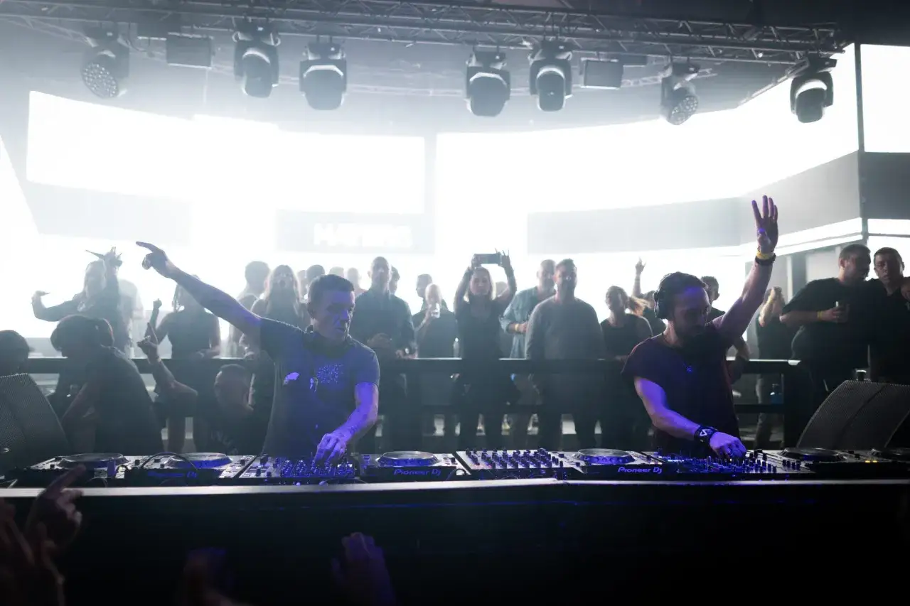 Dj Pepo y su colega animan la multitud en una fiesta con luces brillantes y una energía contagiosa.
