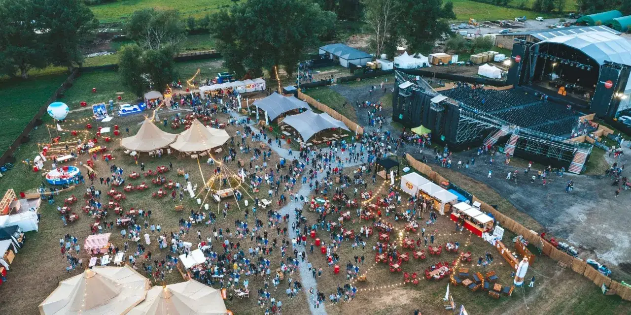 Vista aérea de un festival de música al aire libre, con un gran escenario, carpas, puestos de comida y mucha gente disfrutando del summerfest Cerdanya.