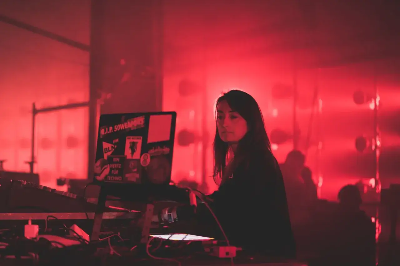 Paula Temple, DJ, concentrada en su set, rodeada de luces rojas y equipos de sonido.