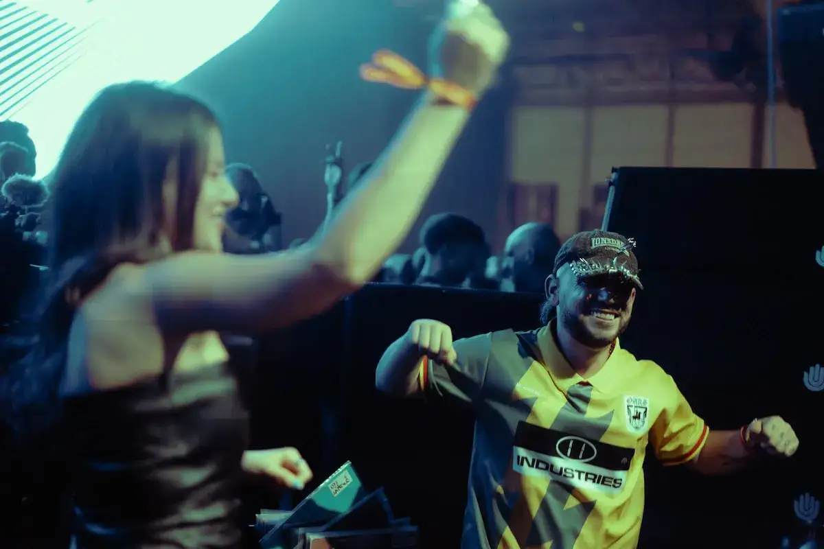 Un hombre sonriente con gorra y camiseta fluor baila animadamente en una fiesta.