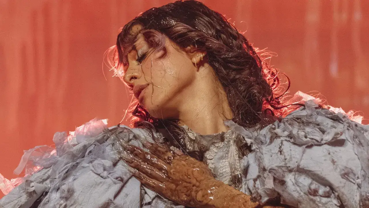 Melanie Martinez, con su característico estilo, anuncia próximos eventos. Su rostro, bañado en luz rojiza, evoca la magia de sus presentaciones.