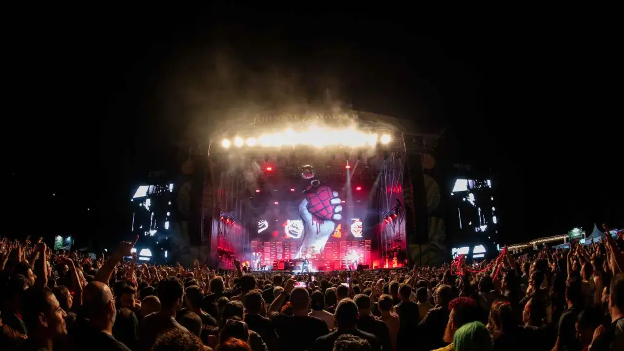 Multitud en concierto de Green Day en Zaragoza, con el icónico logo de granada en el escenario y luces rojas.
