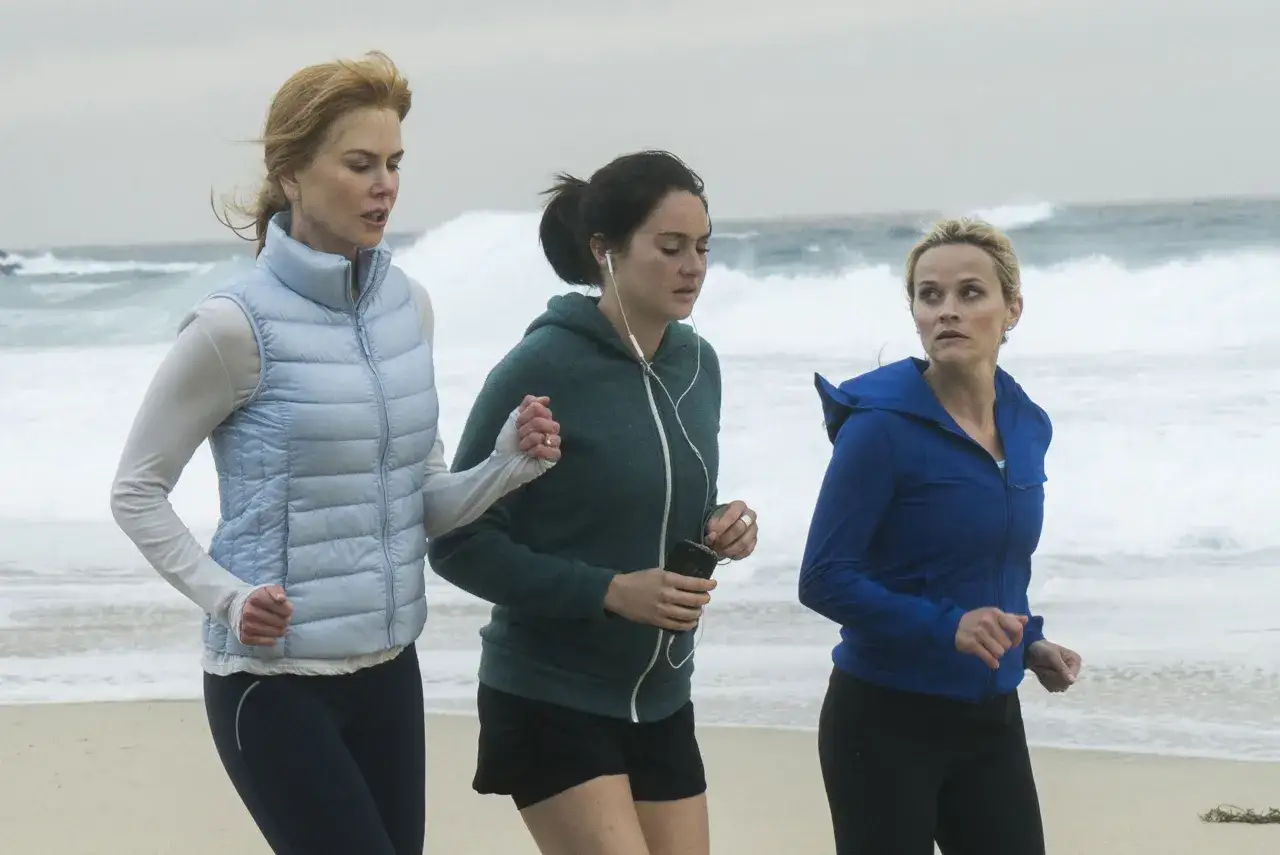 Tres mujeres corren en la playa, con el mar agitado de fondo. Una escena de