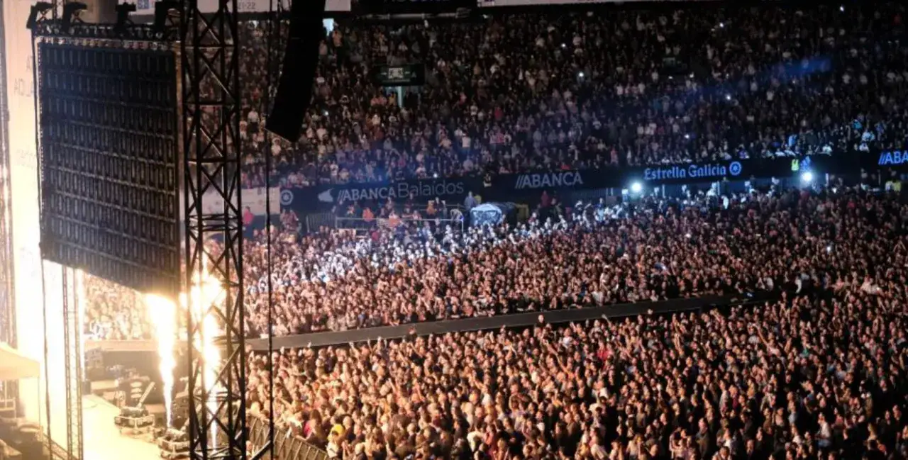 Multitud enloquecida en un concierto de Muse España, con llamas y luces iluminando el escenario.