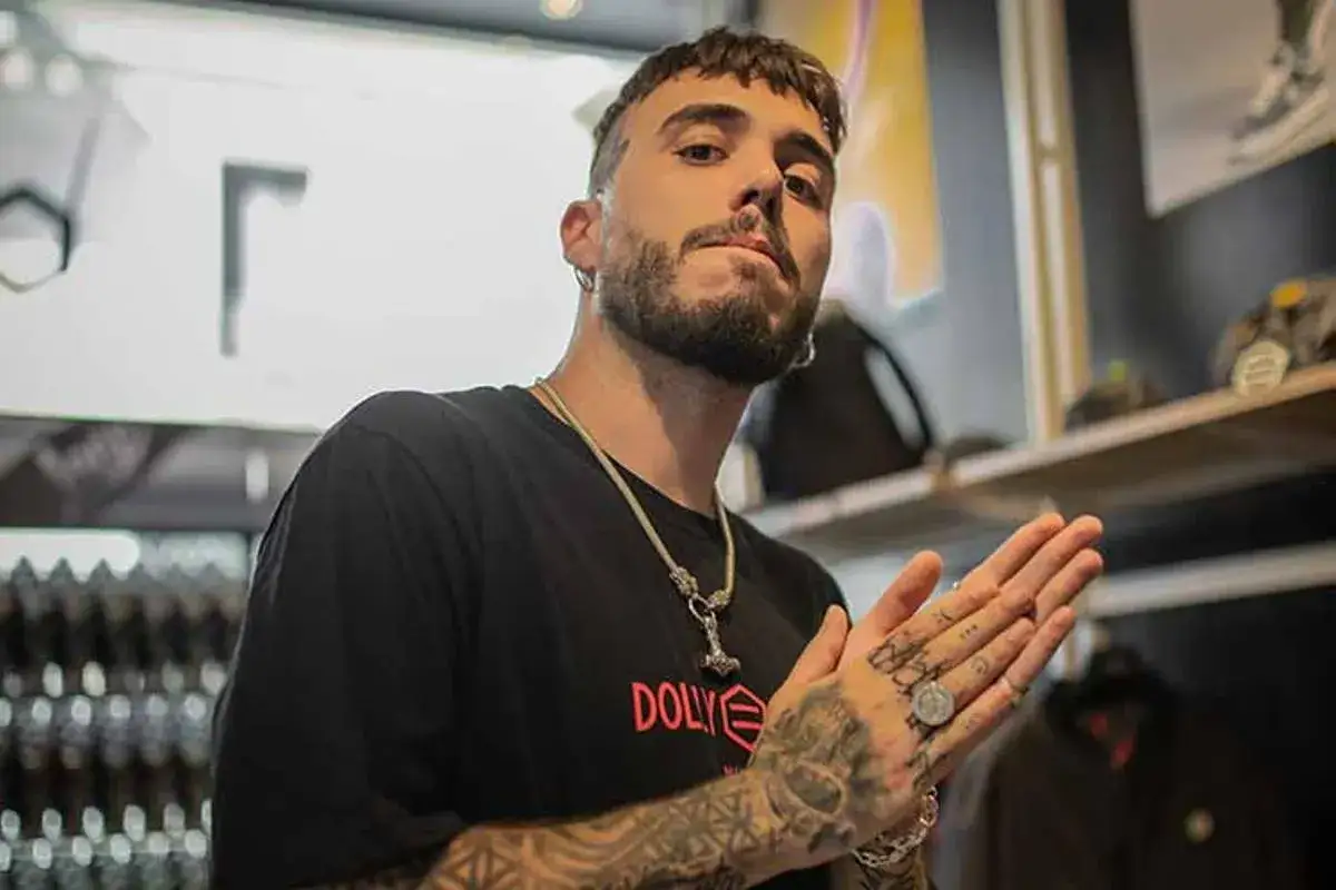 Un hard cantante con tatuajes y un collar llamativo, posa con las manos juntas.