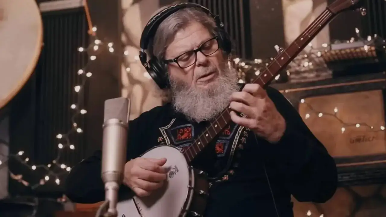 Músico con barba toca el banjo en un estudio, rodeado de luces, creando la banda sonora de The Last of Us.