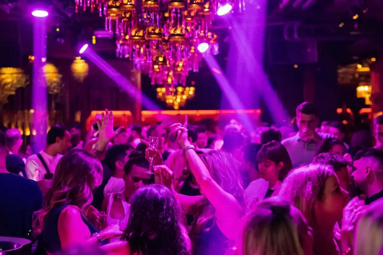 Gente bailando y disfrutando bajo luces moradas y un candelabro dorado. Una noche vibrante en les nits de Barcelona.