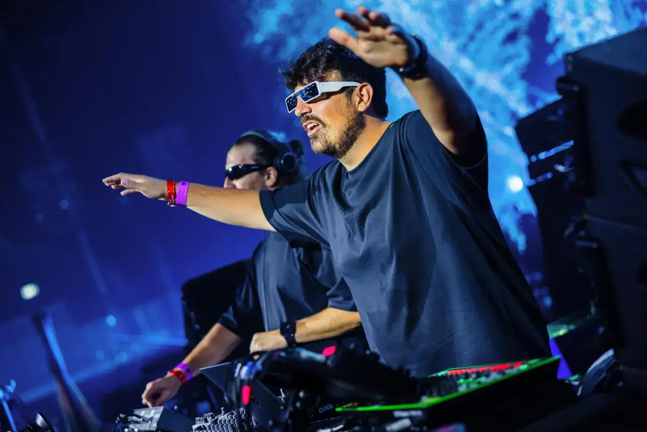 Dos DJs, como agentes del tiempo, manipulan el ritmo en un escenario azul vibrante.