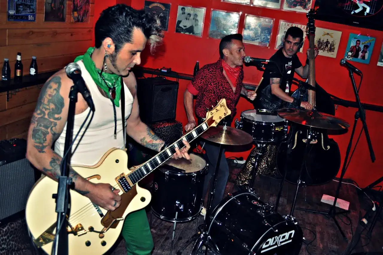 Un grupo de gatos locos en el escenario: guitarrista tatuado, baterista y contrabajista listos para rockear.