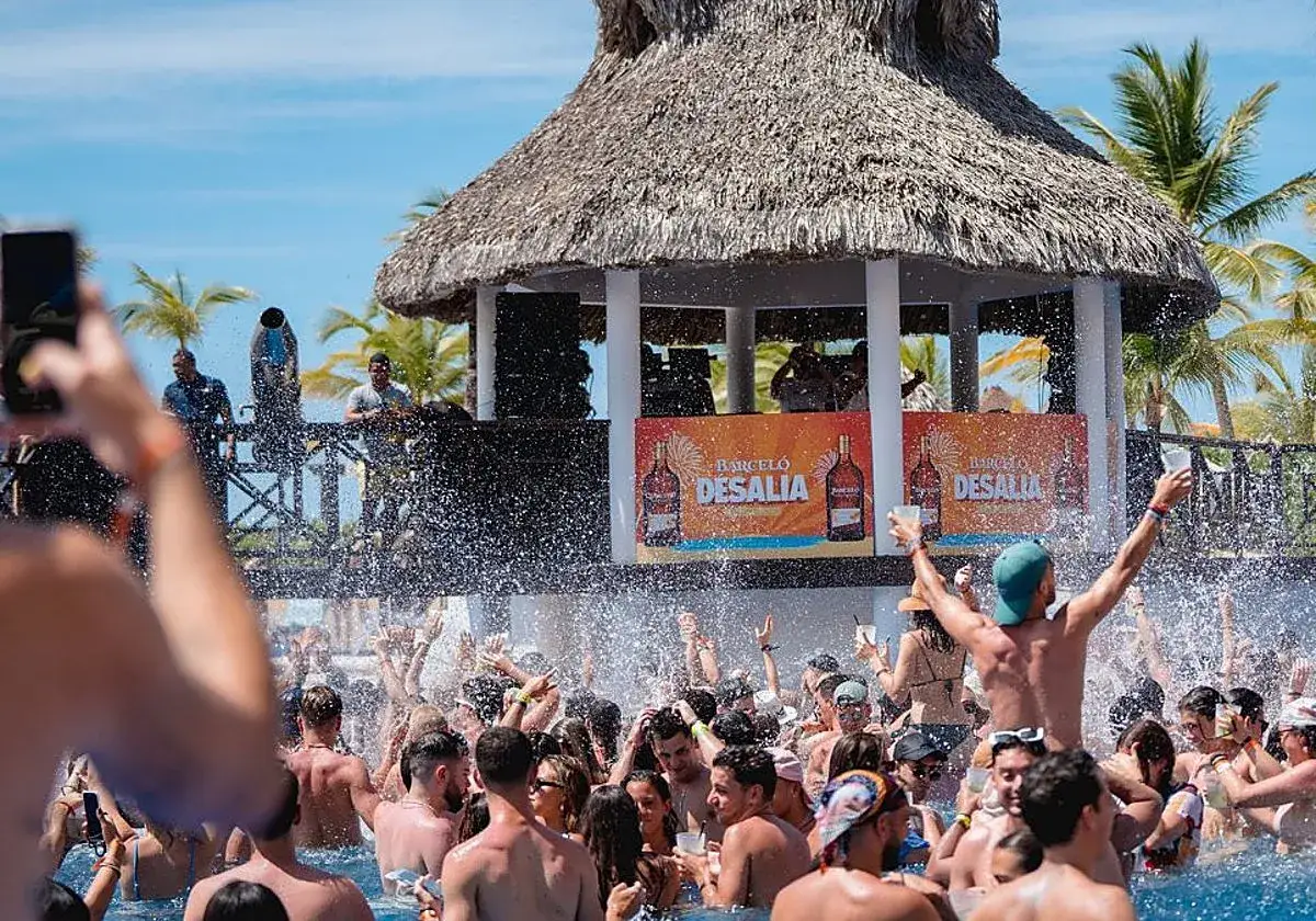 Gente disfrutando en una fiesta en piscina con música y el cartel de Barceló Desalia.