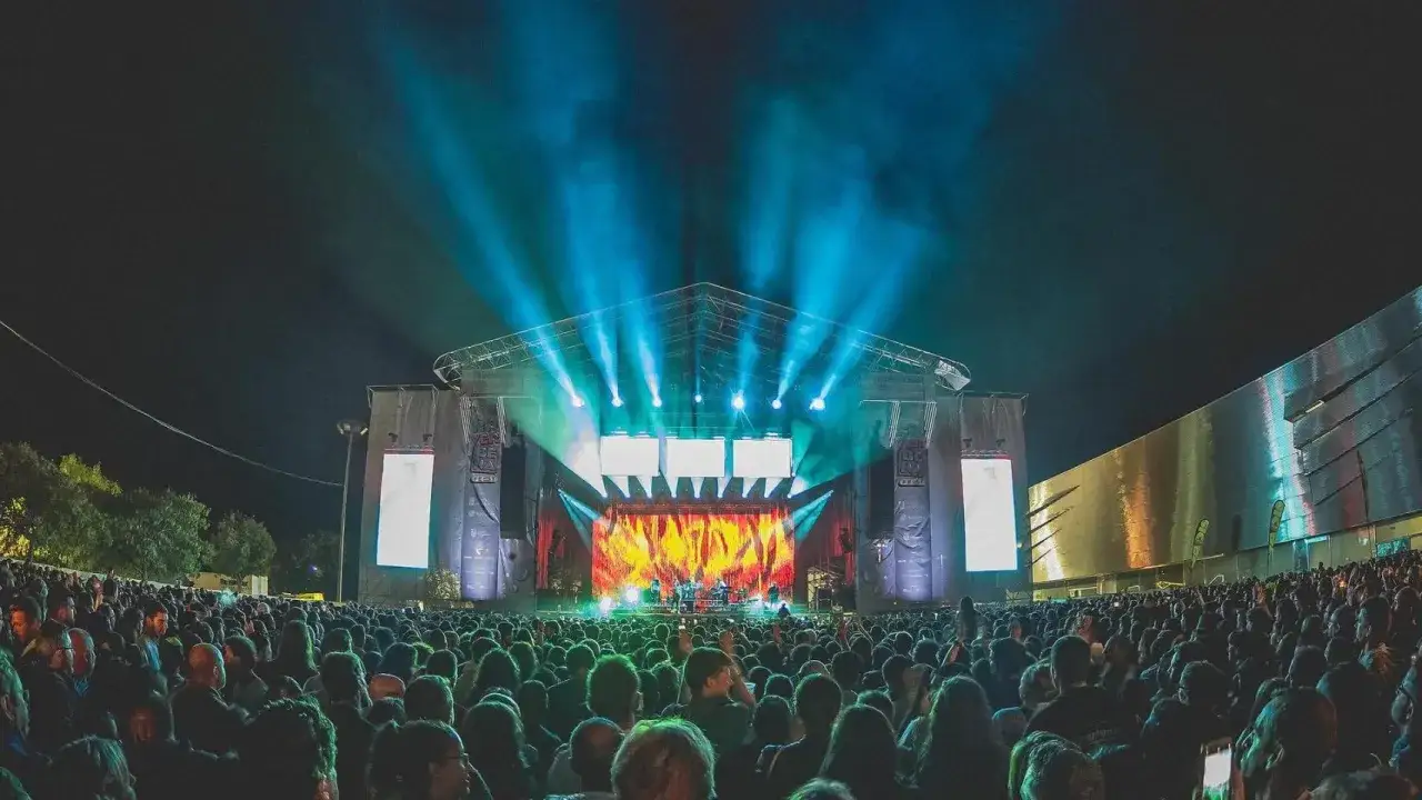 Multitud disfrutando del concierto en el rio verbena fest. Luces azules y amarillas iluminan el escenario.