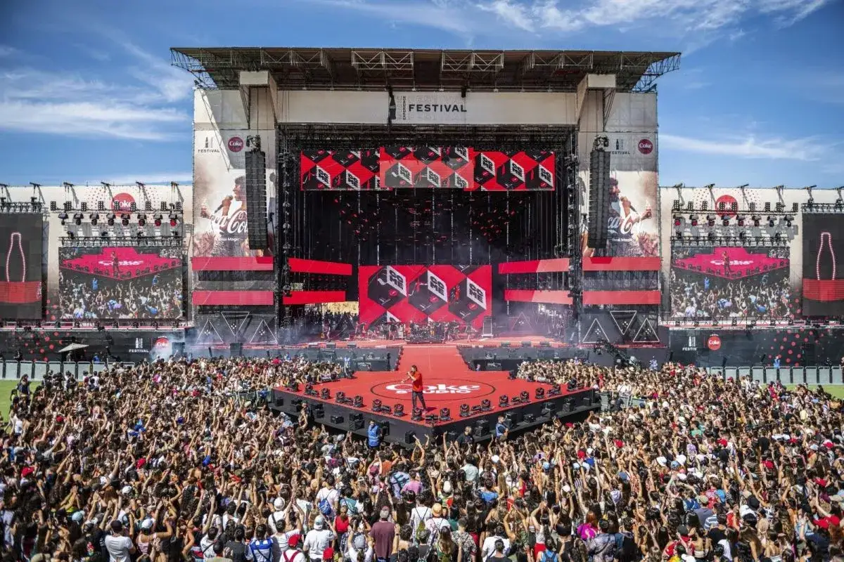 Multitud en el Coca-Cola Music Festival, con un escenario gigante y pantallas mostrando el logo de Coca-Cola.