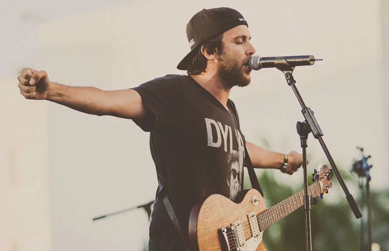 Mario Díaz canta apasionadamente con su guitarra, puño en alto, en un concierto al aire libre.