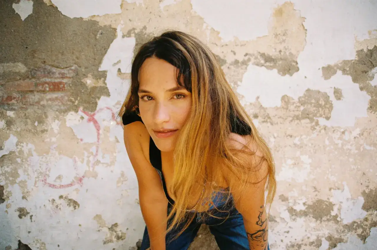 Lia Kali Murcia, con su melena rubia y mirada intensa, posa frente a una pared desconchada.
