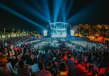 Multitud en un concierto nocturno, luces azules iluminan el escenario y al público. Un evento vibrante, como un **cabaret mairena** moderno.