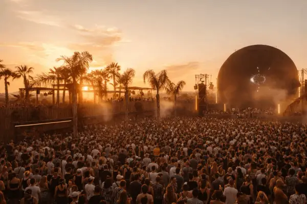 Multitud en el festival Sophie, disfrutando del atardecer con palmeras y una gran esfera como escenario.
