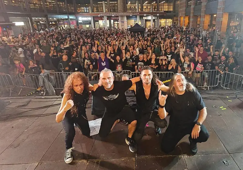 La banda Syberia posa con su público. Los músicos, con atuendos oscuros, se arrodillan mientras una multitud enardecida los aclama.