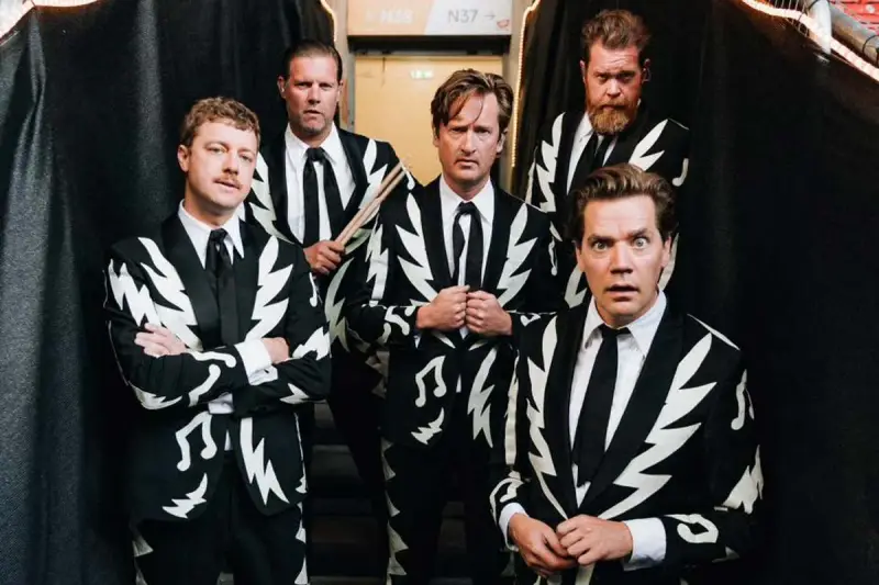 Los miembros de The Hives posan con trajes llamativos. Uno sostiene baquetas, listo para la acción.